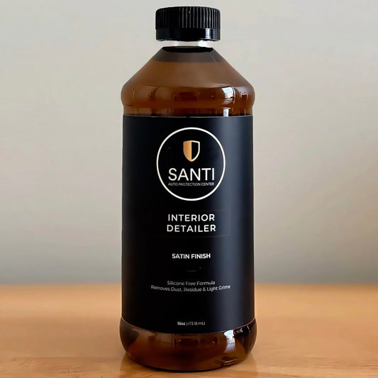 A 500ml bottle of Santi Interior Detailer in satin finish, featuring a black label and black cap, set on a wooden surface against a neutral background.
