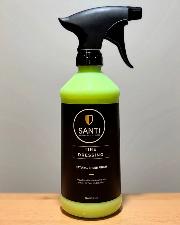 A bottle of SANTI Tire Dressing in Natural Green Formula, featuring a bright neon green liquid and a black spray nozzle, set on a wooden surface against a neutral gray background.