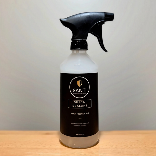 A bottle of SANTI Silica Sealant with a black spray trigger top and a black label, sitting on a light wood surface against a neutral beige background.