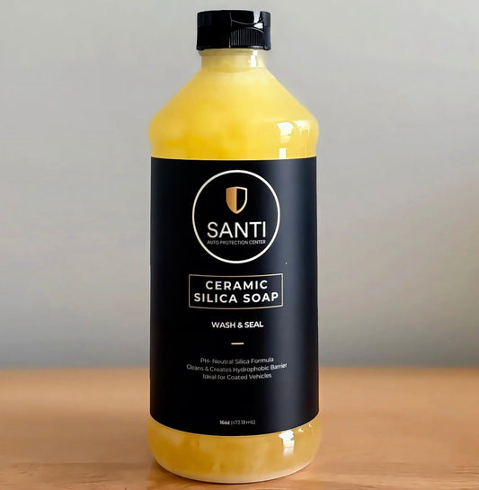 A bottle of Santi Ceramic Silica Wash & Seal soap in a translucent yellow container with a black cap and black label, sitting on a wooden surface against a neutral gray background.