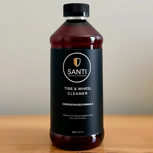 A bottle of Santi Tire & Wheel Cleaner with a black cap and black label, placed on a wooden surface against a neutral beige background.