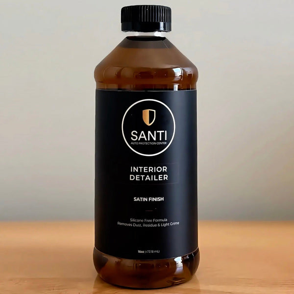 A 500ml bottle of Santi Interior Detailer in satin finish, featuring a black label and black cap, set on a wooden surface against a neutral background.