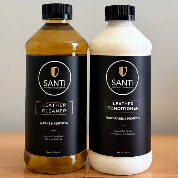 Two bottles of Santi Leather Care products on a wooden surface against a neutral beige background: a 500ml bottle of Leather Cleaner filled with amber liquid, and a 500ml bottle of Leather Conditioner with a white liquid.