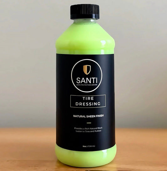 A bottle of Santi Tire Dressing in a bright neon yellow-green color with a black cap and a black label, sitting on a wooden surface against a neutral gray background.